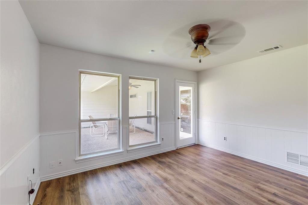 Wood-finish flooring, white paneled wainscoting, multiple windows, a ceiling fan, and a glass-paneled exterior door