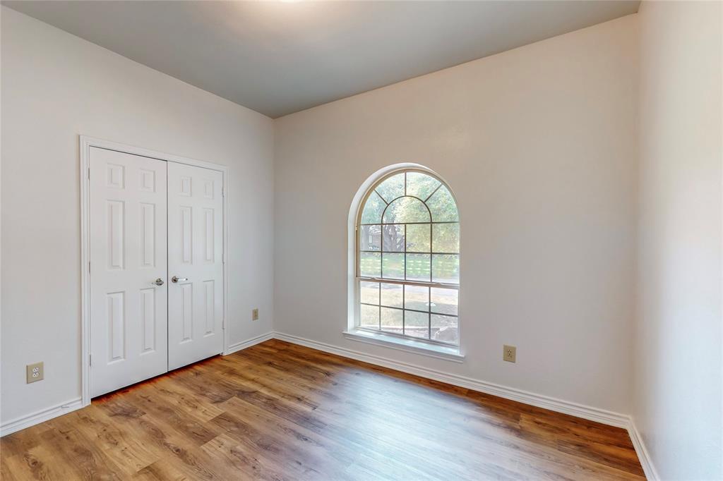 Arched window with gridded panes, wood-finish flooring, paneled bifold closet doors, and white trim