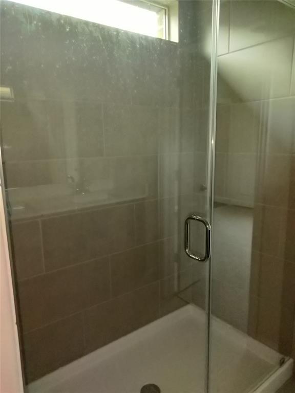 Frameless glass shower enclosure with a chrome handle, complemented by large format wall tiling and a white shower pan