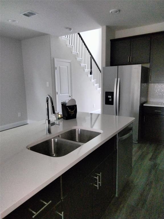 Kitchen island with an undermount double basin stainless steel sink, a pull-down faucet, light-toned countertop, and dark cabinetry