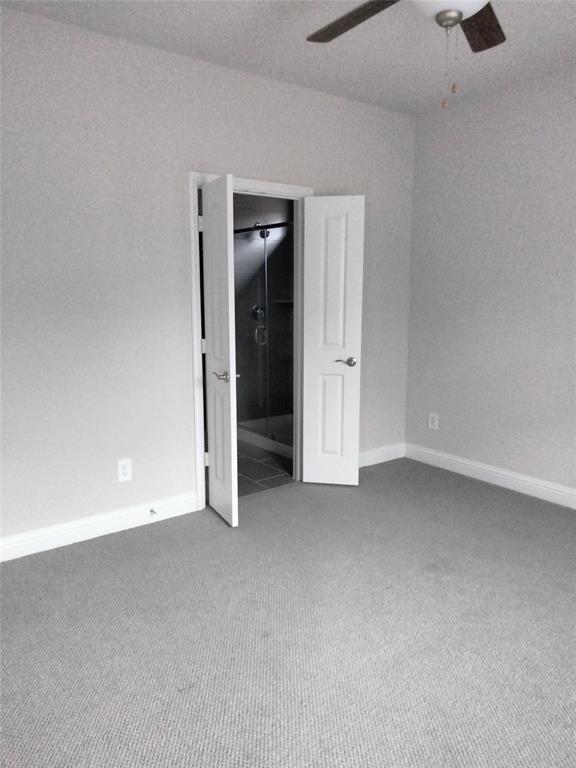 Carpeted flooring, light gray wall paint, white trim, ceiling fan, and an open doorway to a tiled shower area