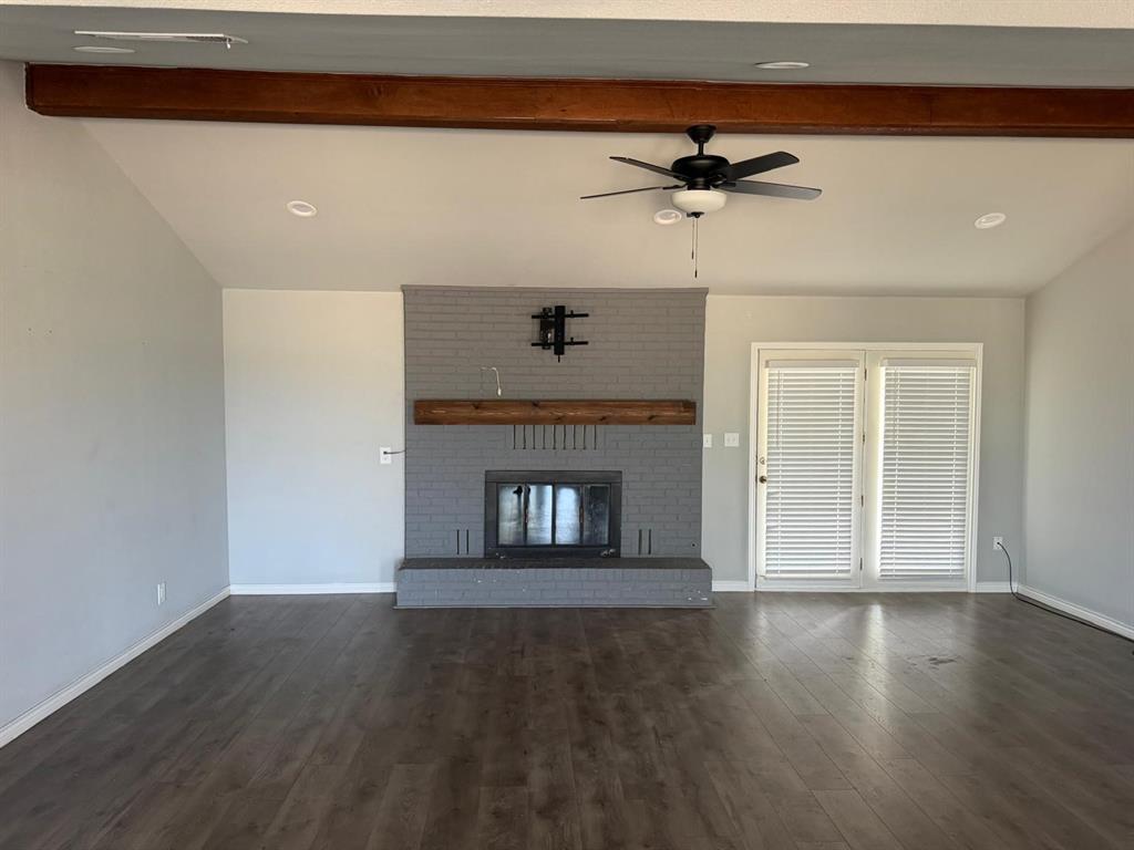 Spacious living area featuring wood-finish flooring, a painted brick fireplace with a wood mantle, exposed wood beams, a ceiling fan, and recessed lighting