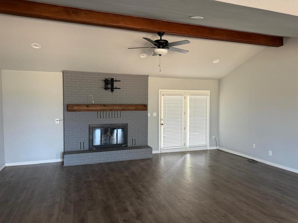 Vaulted ceiling with exposed wood-finish beam, brick fireplace with wood-finish mantel, wood-finish flooring, and double French doors
