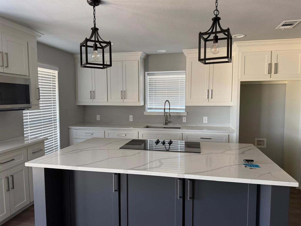Kitchen featuring white upper and lower cabinetry, a dark-toned island with a light-toned countertop, and two pendant light fixtures