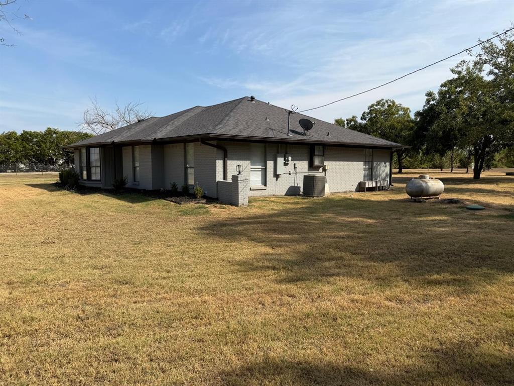 Single-story exterior with a dark shingle roof, light-colored brick siding, and an expansive yard Single-story exterior with a dark shingle roof, light-colored brick siding, and an expansive yard
