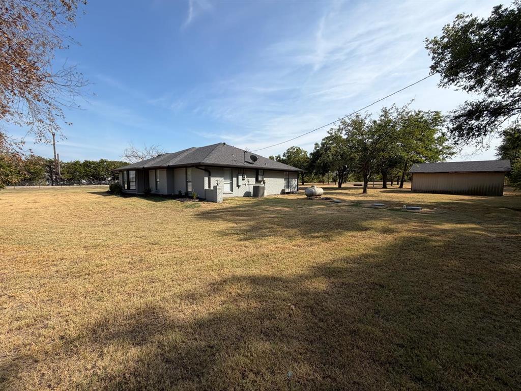 Single-story residence with a gray shingle roof, light-colored exterior siding, multiple windows, and a detached outbuilding Single-story residence with a gray shingle roof, light-colored exterior siding, multiple windows, and a detached outbuilding