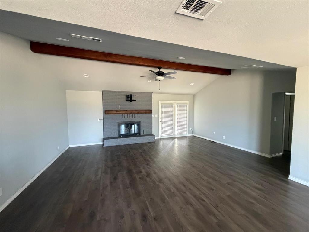 Vaulted ceiling with an exposed wood beam, wood-finish flooring, brick fireplace with a wood mantel, and double French doors