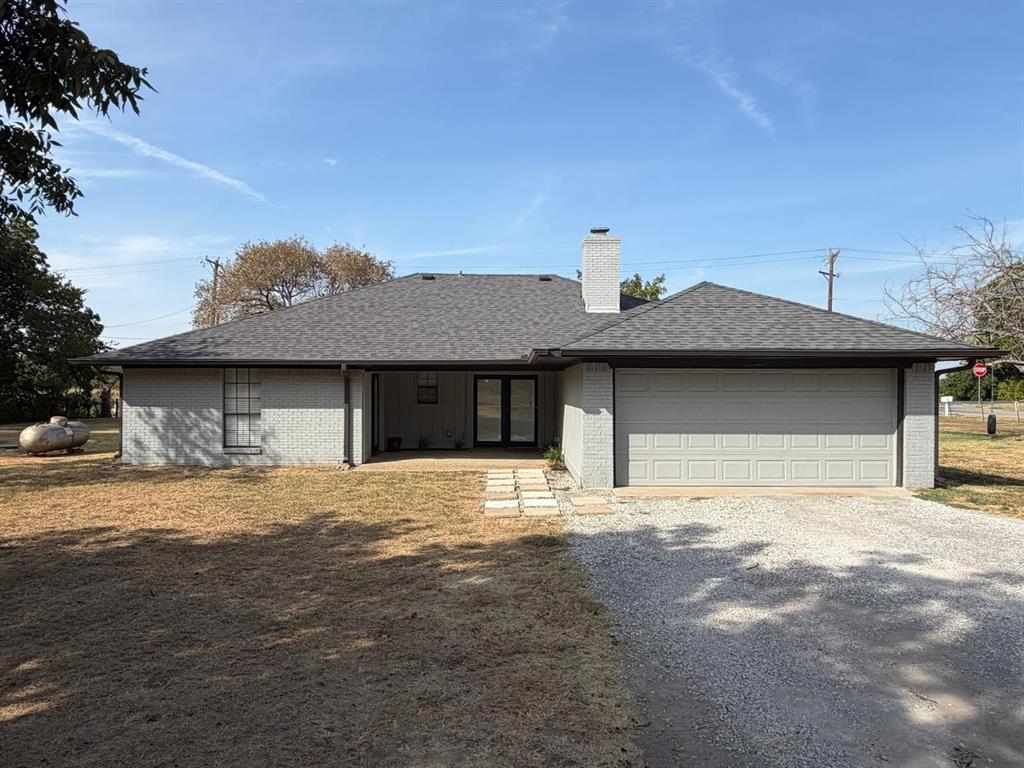 Grey brick exterior with a dark shingled roof, attached two-car garage, and a covered entry Grey brick exterior with a dark shingled roof, attached two-car garage, and a covered entry