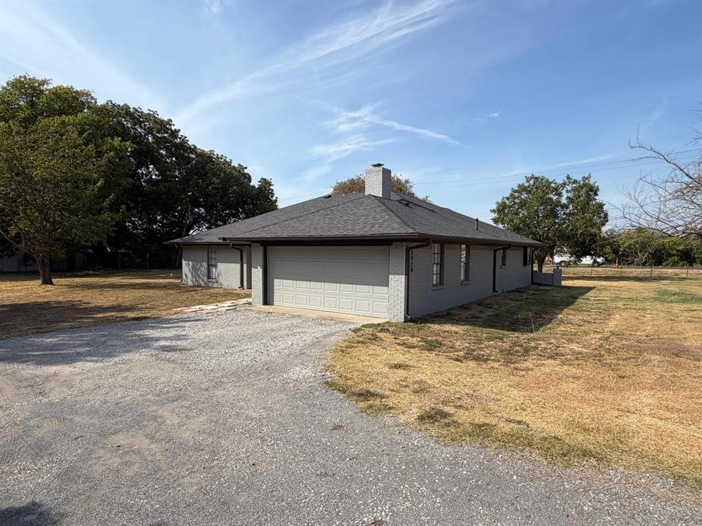 Single-story residence with a gray exterior, a dark shingle roof, and a gravel driveway Single-story residence with a gray exterior, a dark shingle roof, and a gravel driveway