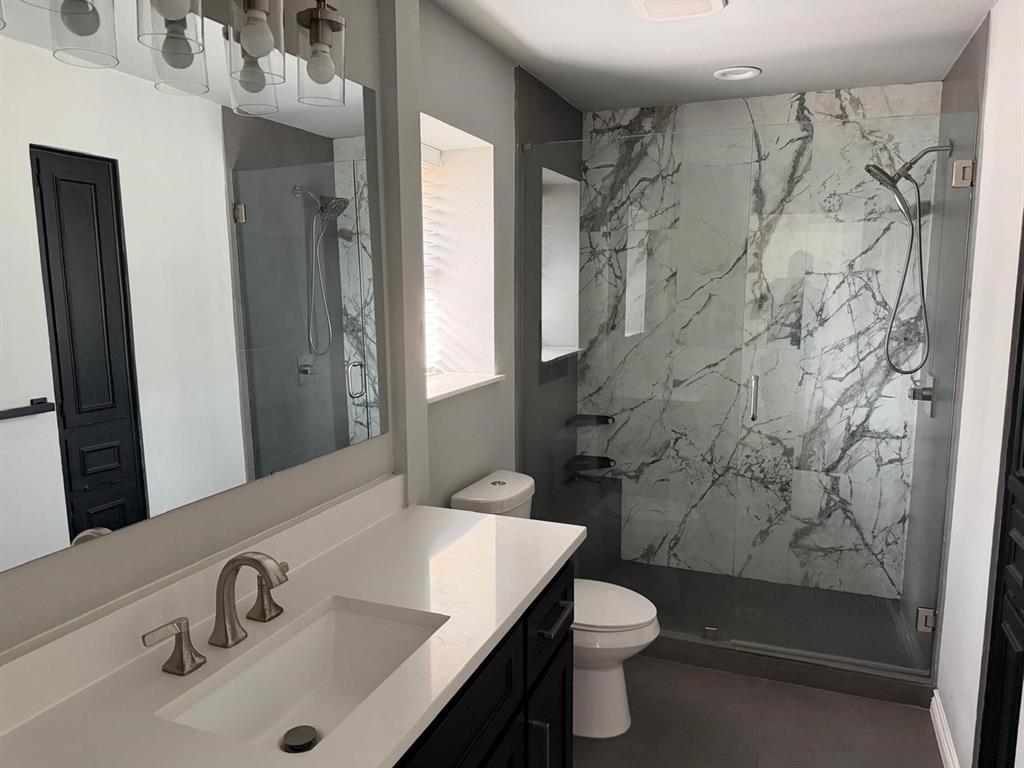 Custom glass-enclosed shower with large format marble-look tile, fixed and handheld showerheads, and recessed shelving