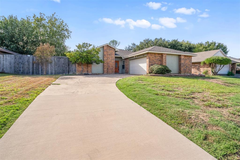 Single-story brick exterior featuring a multi-car attached garage, concrete driveway, and wooden privacy fencing
