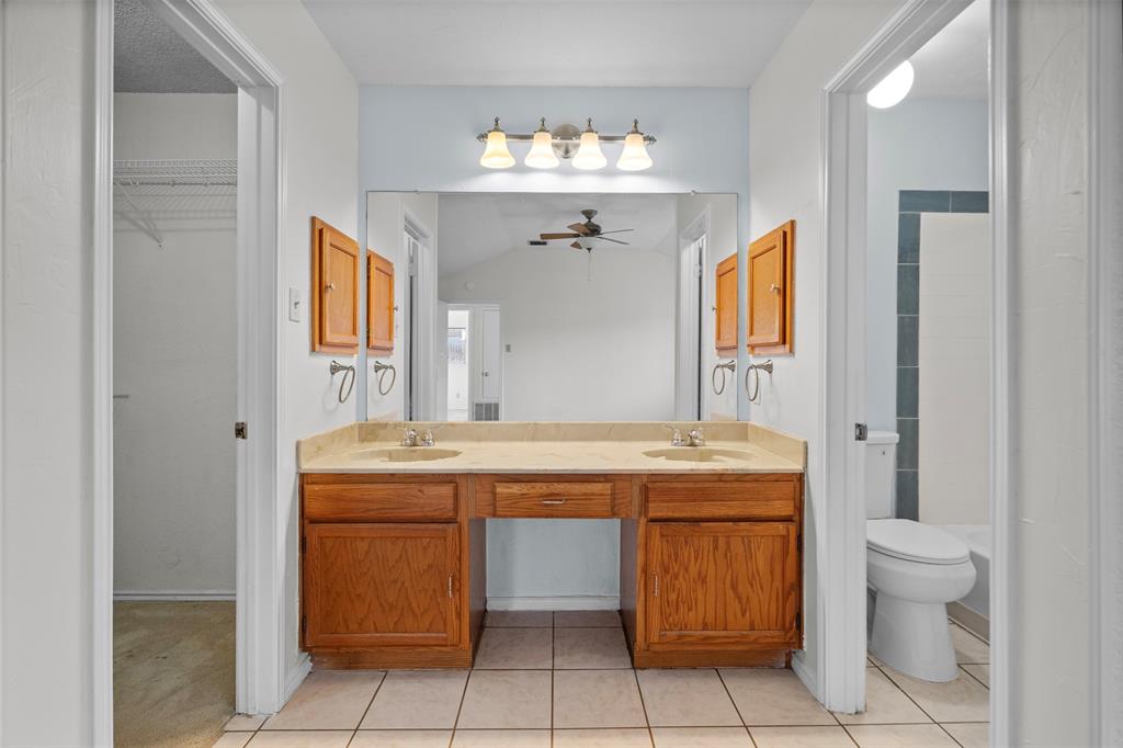 Double vanity featuring wood cabinetry, a dual-basin countertop, a full-width mirror, and four-light vanity fixture