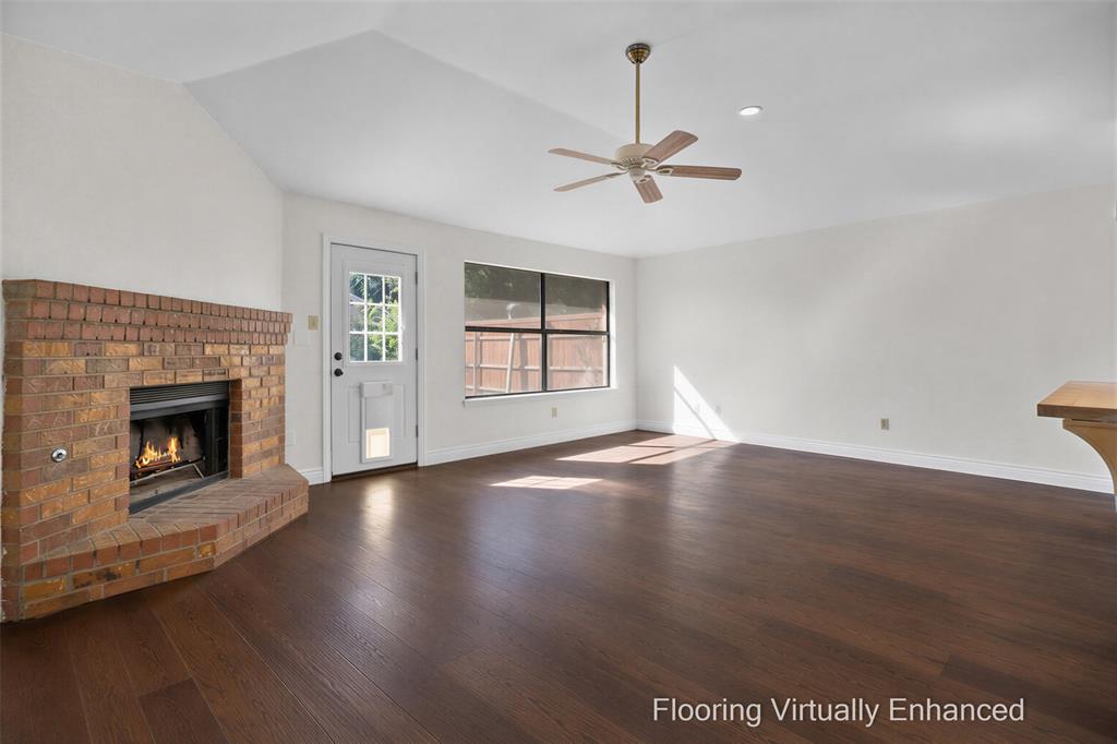Vaulted ceiling with an integrated light fixture, wood-finish flooring, and a brick fireplace featuring a raised hearth