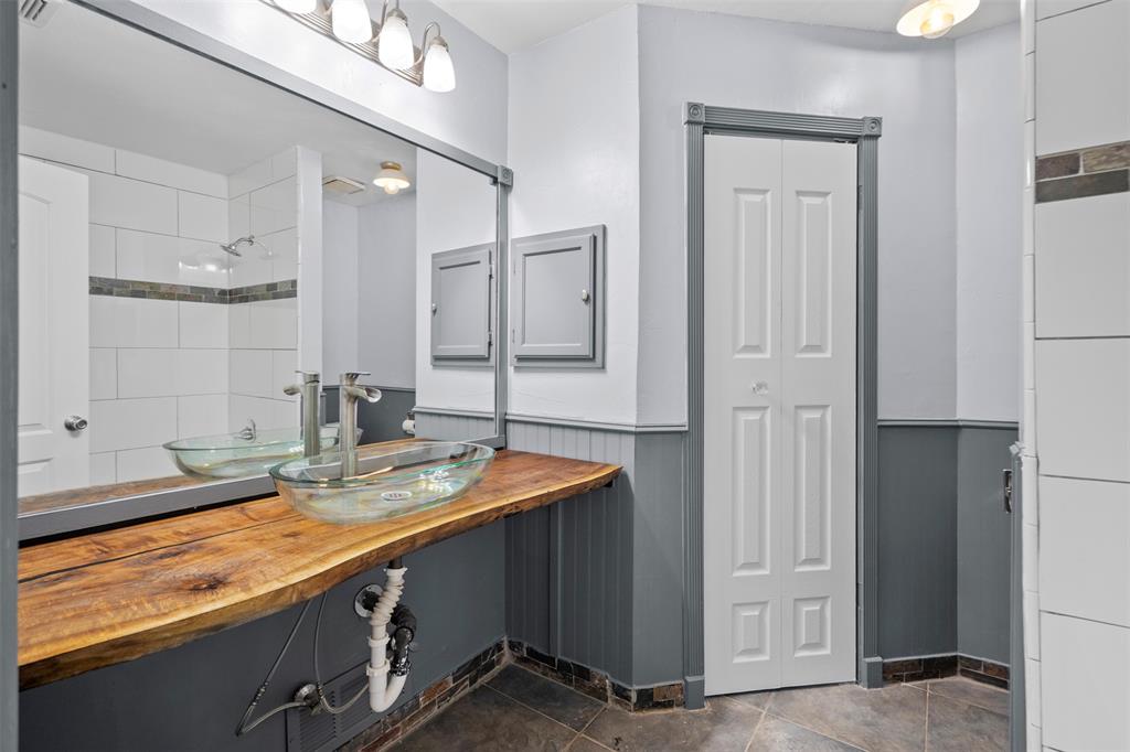 Live-edge wood countertop featuring a glass vessel sink, chrome faucet, wall-to-wall mirror, wainscoting, and ceramic tile flooring