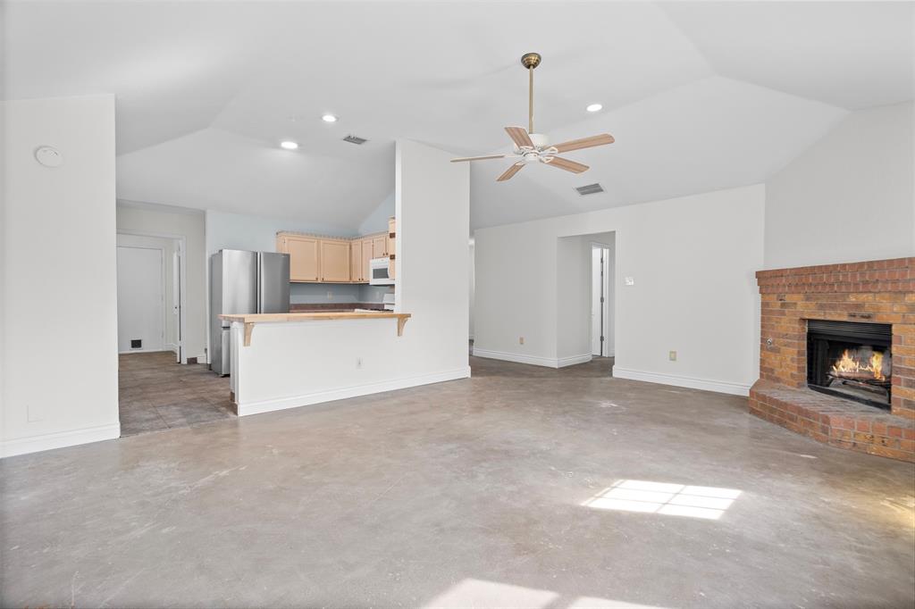 Vaulted ceilings featuring a central ceiling fan, brick fireplace with a raised hearth, and neutral concrete flooring