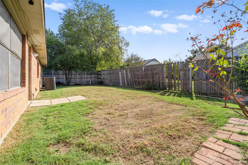 Backyard featuring a brick exterior wall, wood privacy fencing, grass lawn, and masonry paver pathways