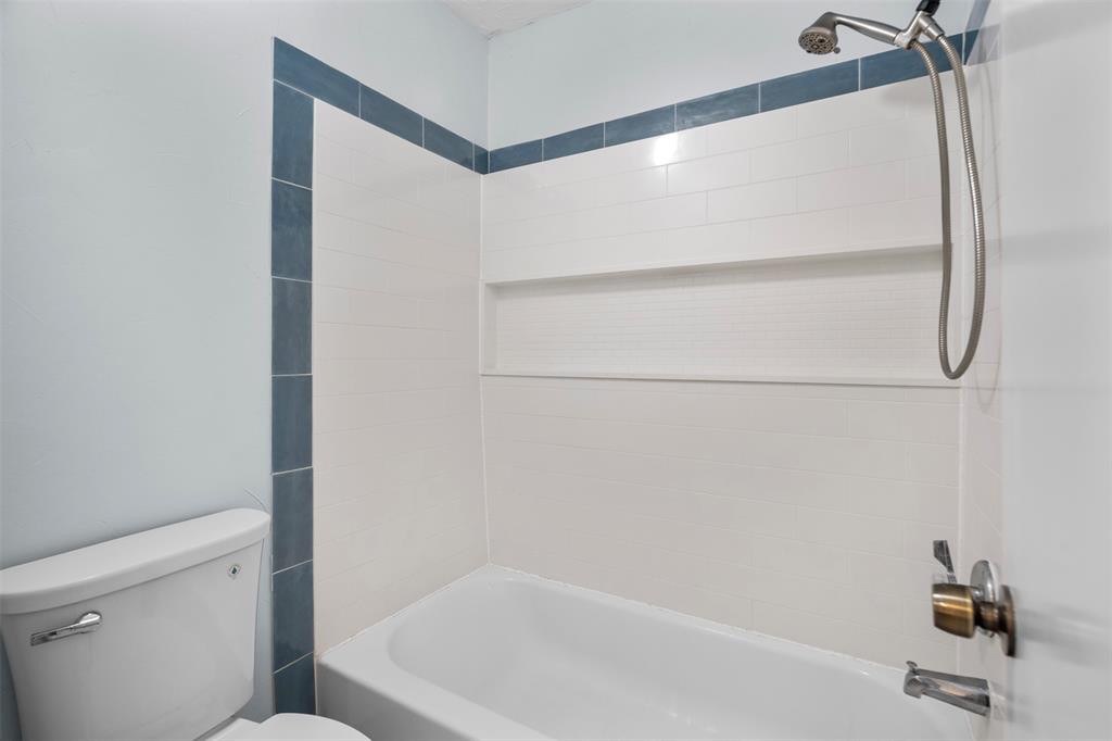 Shower and tub combination featuring white rectangular wall tile with blue accent trim, integrated horizontal storage niche, and silver-tone handheld shower fixture