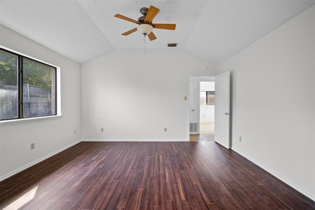 Vaulted ceiling featuring a central wood-blade ceiling fan with integrated light fixture, complemented by dark wood-finish flooring and a single-pane window