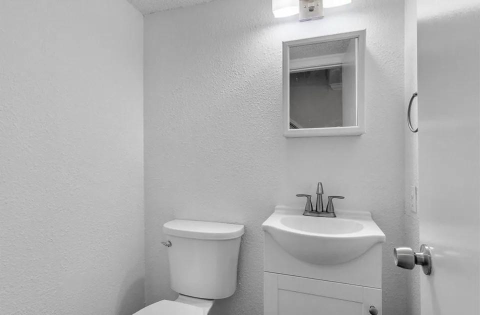 A bright white half bathroom showcasing a toilet, a modern vanity with a simple mirror on the wall.