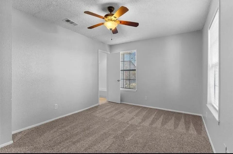 A cozy bedroom featuring a neutral-colored carpet, ceiling fan and tall windows, creating a comfortable atmosphere.
