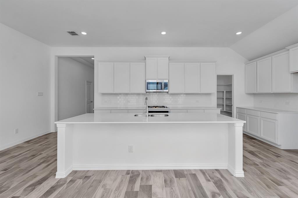 Kitchen with stainless steel microwave, a kitchen island with sink, decorative backsplash, light countertops, and lofted ceiling