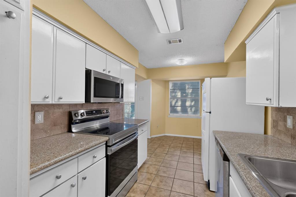 Kitchen featuring white cabinetry, stainless steel appliances, granite-look countertops, a tiled backsplash, and tile flooring