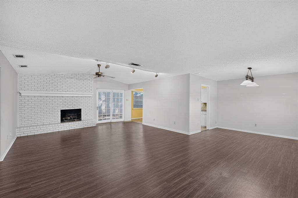 Wood-finish flooring throughout, white brick fireplace with a mantel, vaulted ceiling, ceiling fan, and double glass doors