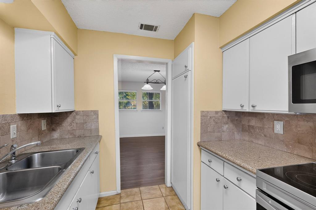 White cabinetry with chrome hardware, dual basin stainless steel sink, stone countertops, and a tiled backsplash