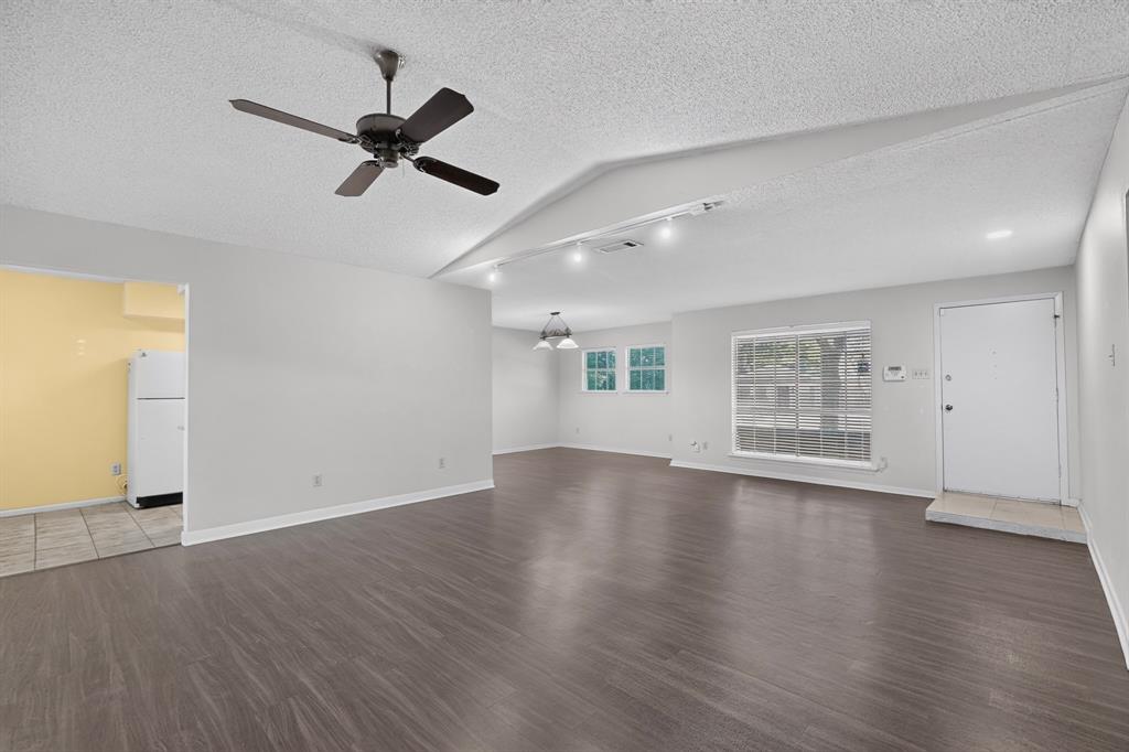 Vaulted ceiling with an installed ceiling fan, wood-finish flooring, two large windows, white walls, and track lighting