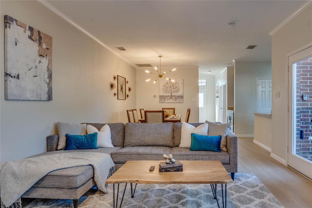 Open-concept living space with crown molding, wood-finish flooring, and a modern chandelier