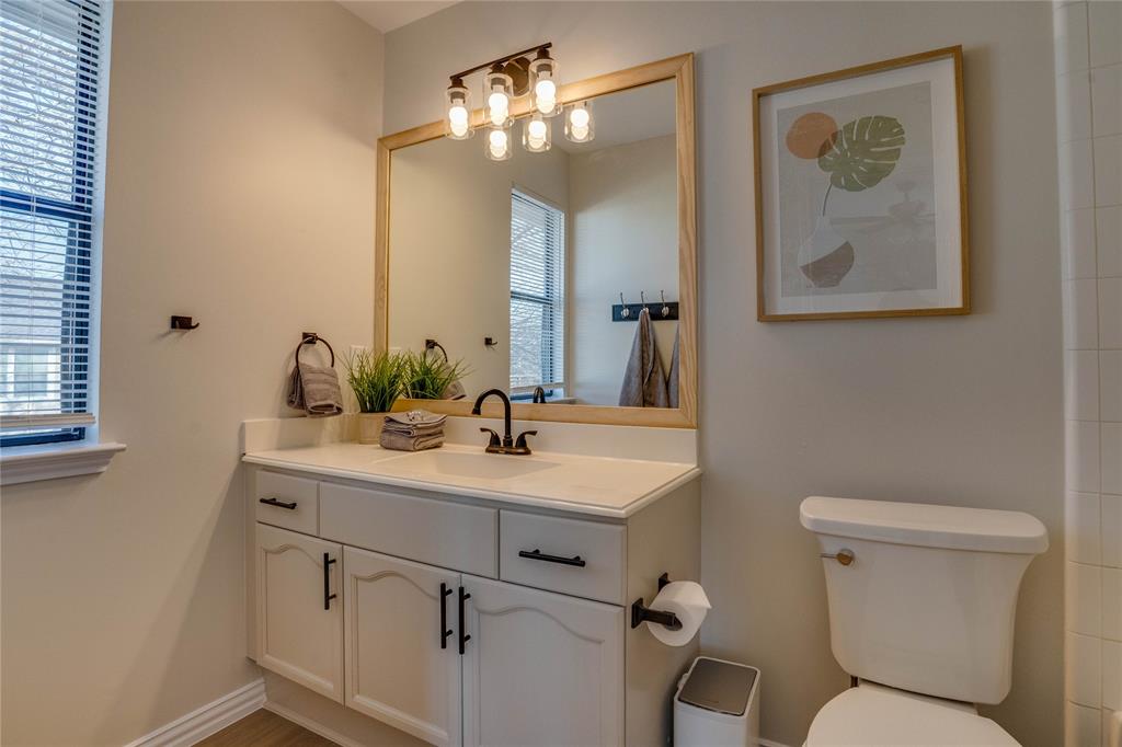 Vanity with white cabinetry, countertop, and an integrated sink, featuring a wood-framed mirror with a four-bulb light fixture
