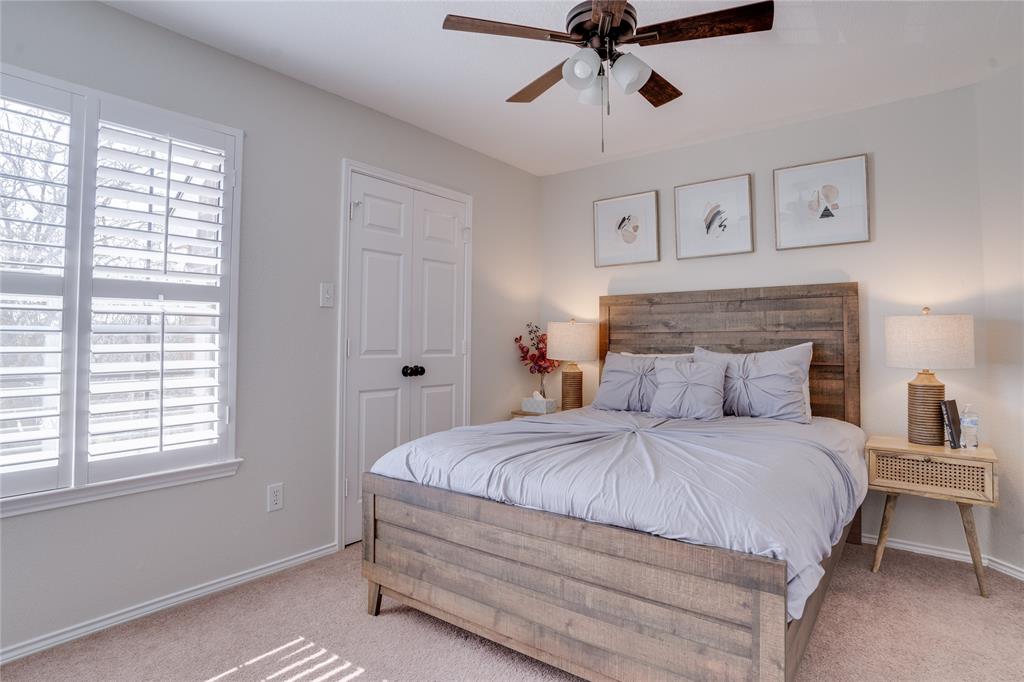 Hardwood ceiling fan with integrated lighting, window with plantation shutters, light-toned carpeting, and a double-door closet