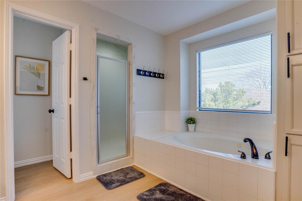Spa-inspired primary bathroom featuring a soaking tub with deck-mounted faucet, wood-finish flooring, and abundant natural light from a large picture window