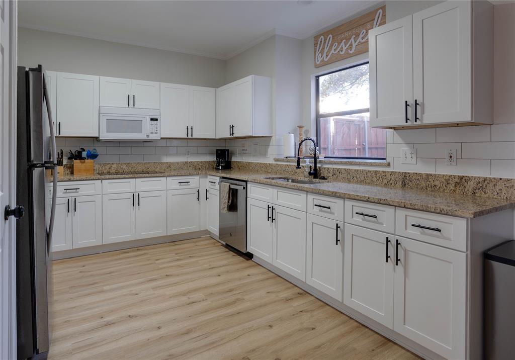 Kitchen featuring white cabinetry, light-toned wood-finish flooring, a stainless steel dishwasher, a black refrigerator, and a window above the sink