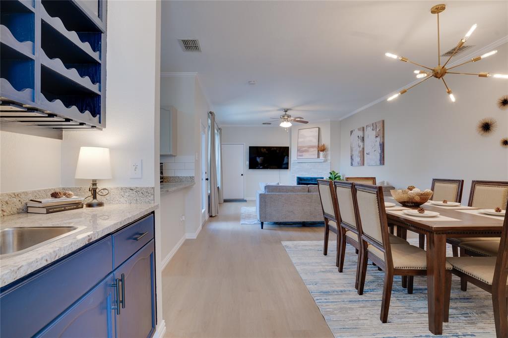 Open-concept living space featuring wood-finish flooring, a contemporary chandelier, and a built-in wet bar with blue cabinetry and a stainless steel sink