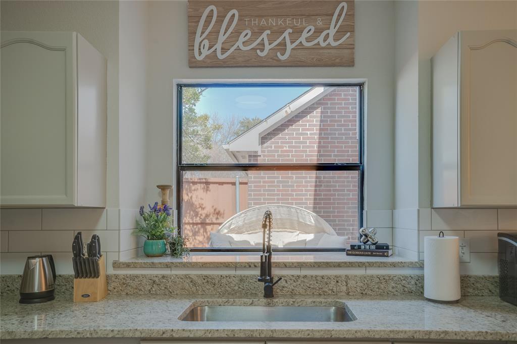 Stainless steel sink with a matte black faucet, light granite countertops, white subway tile backsplash, and white upper cabinetry