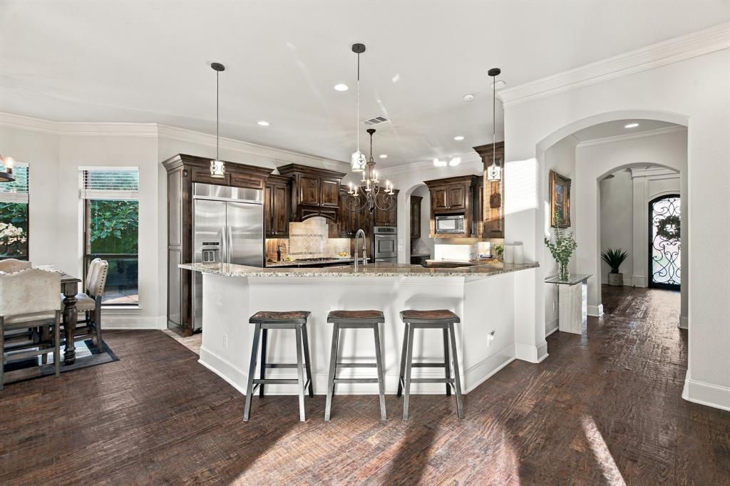 Kitchen featuring dark wood cabinetry, stainless steel appliances, stone countertops, wood-finish flooring, and crown molding