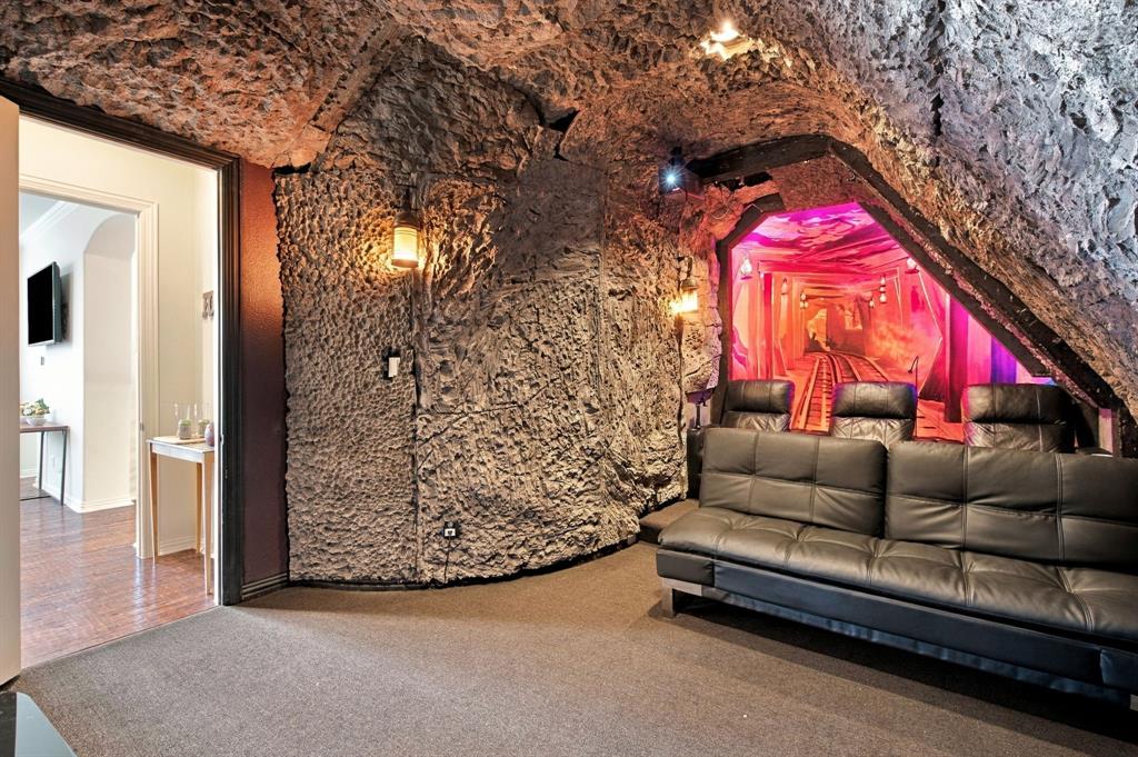 Textured stone wall detailing, dramatic cavern-inspired ceiling, wall-mounted metal light fixtures, and wall-integrated graphic mural