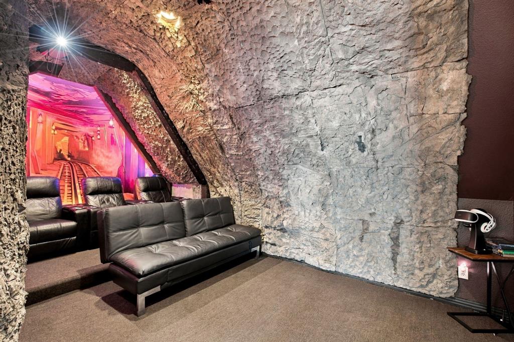 Media room featuring textured rock-finish walls, arched ceiling structure, and stepped flooring