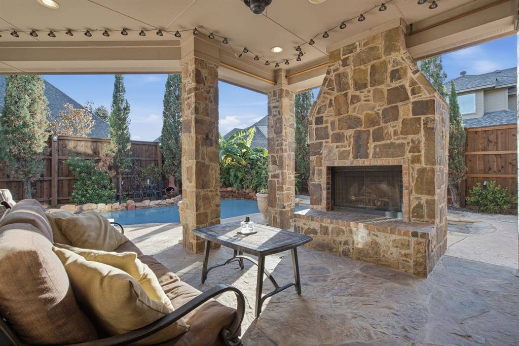 Covered patio featuring a floor-to-ceiling stone fireplace, stone masonry pillars, and natural stone flooring