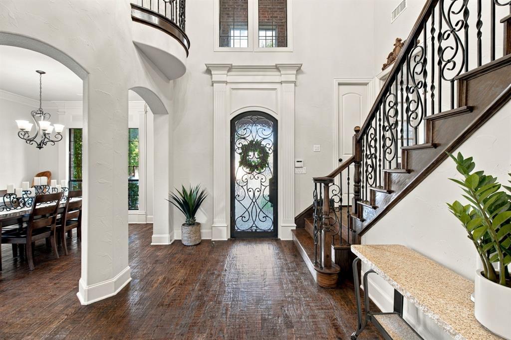 Grand foyer featuring a custom wrought-iron entry door, sweeping staircase with intricate metal balusters, polished wood-finish flooring, soaring ceilings, and arched architectural entryways