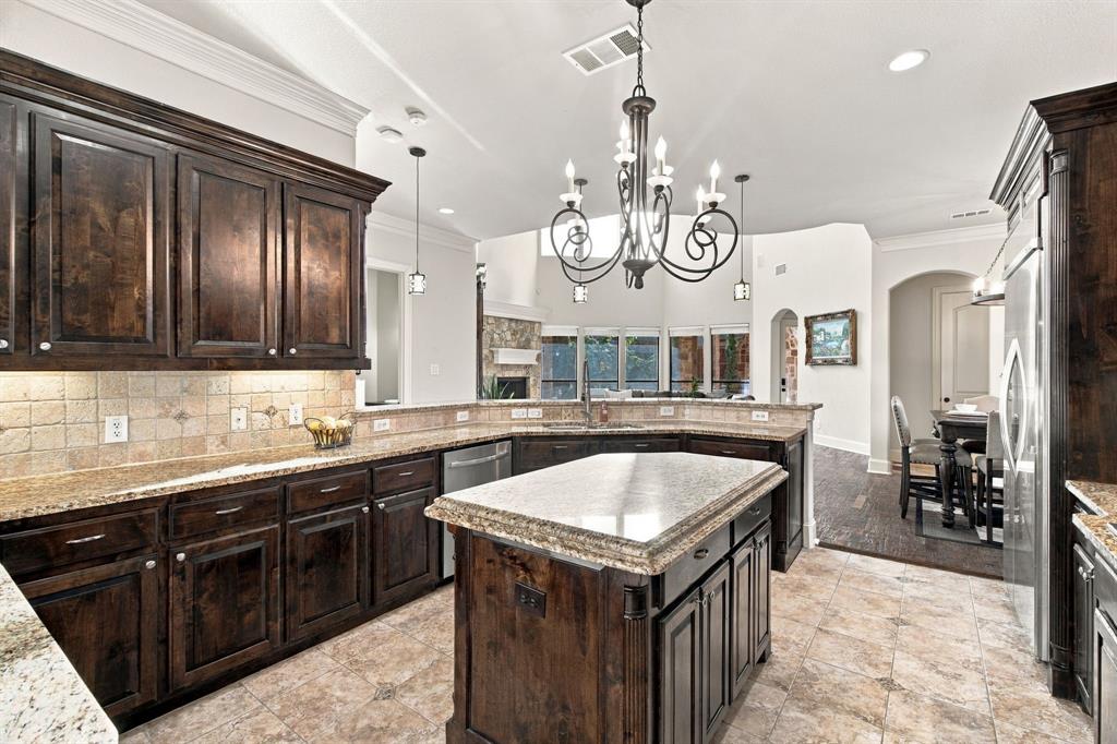 Kitchen featuring dark-finish cabinetry, natural stone countertops, a central island, tiled flooring, and a decorative wrought iron chandelier
