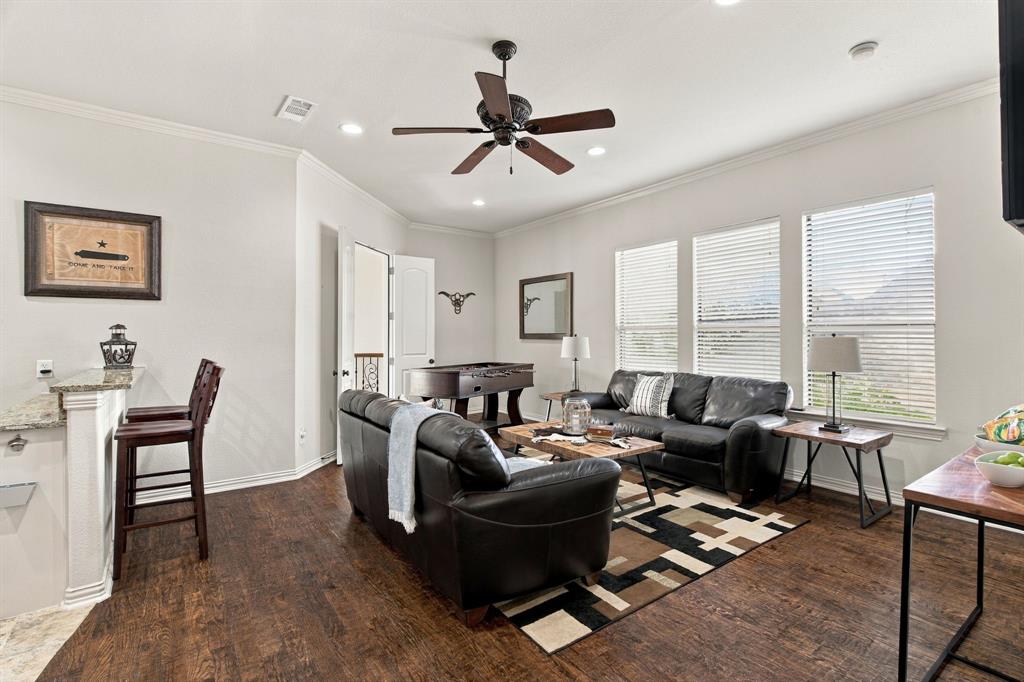 Open-concept room featuring dark wood-finish flooring, recessed lighting, a ceiling fan, and a built-in bar with stone-finish countertops