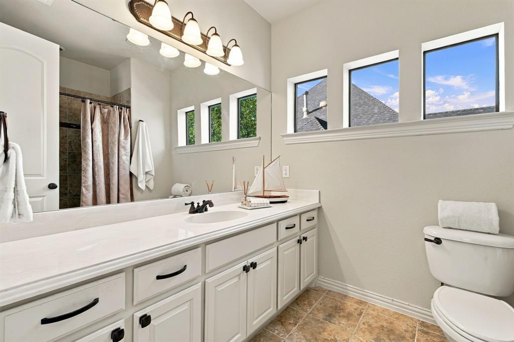 Double vanity featuring white cabinetry, a solid-surface countertop, an integrated sink with dark metal hardware, and full-width wall-mounted mirror