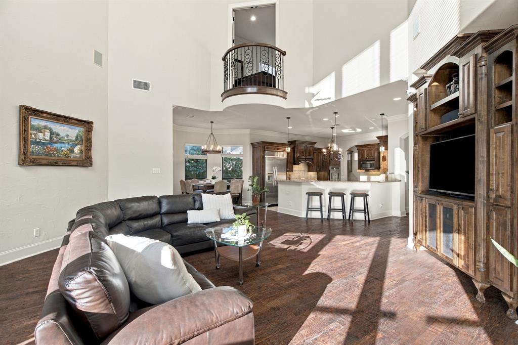 Two-story high ceiling with interior wrought-iron Juliet balcony, custom built-in dark wood cabinetry, wood-finish flooring, and recessed lighting