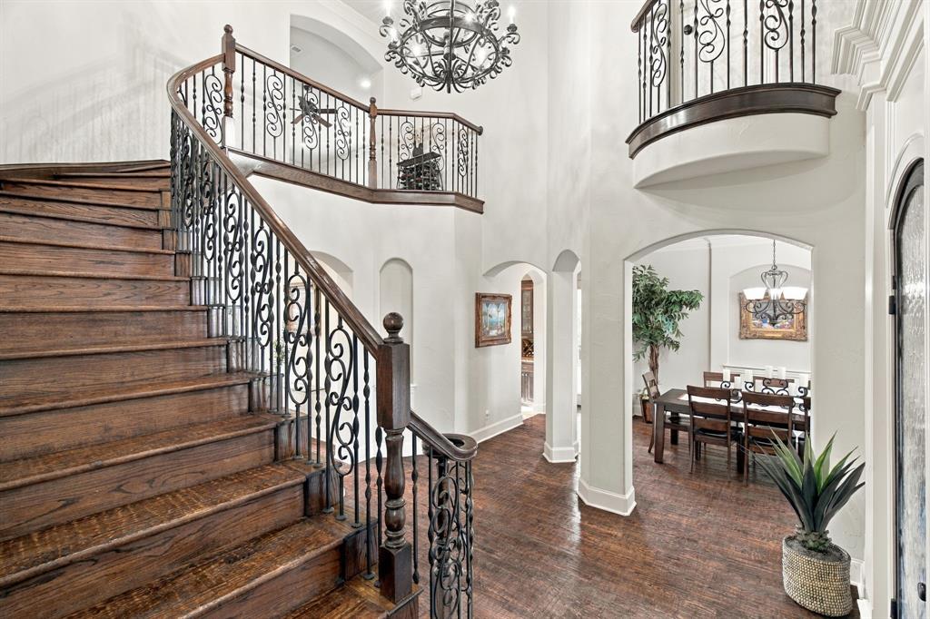 Grand foyer featuring a curved staircase with wood treads and ornate metal balusters, polished wood-finish flooring, soaring ceilings, a decorative chandelier, and arched architectural entryways
