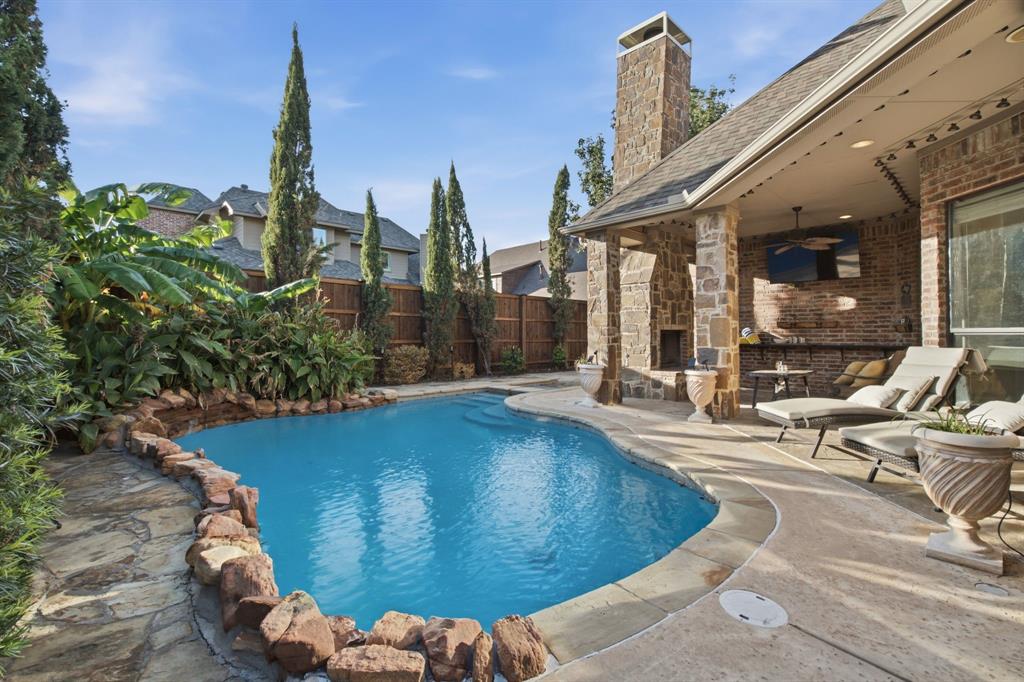 Outdoor living area featuring a covered patio with a stone-surround fireplace, an in-ground swimming pool with rock edging, and flagstone hardscaping