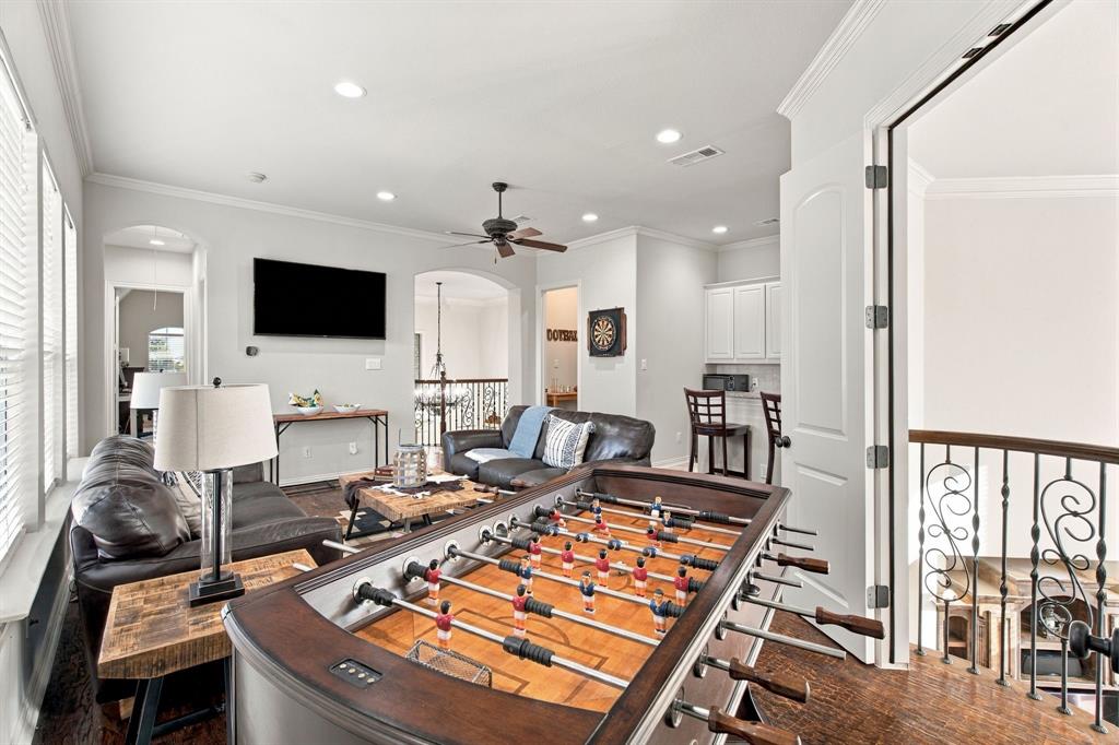 Open-concept living space featuring wood-finish flooring, recessed lighting, crown molding, arched entryways, and wrought iron balustrades