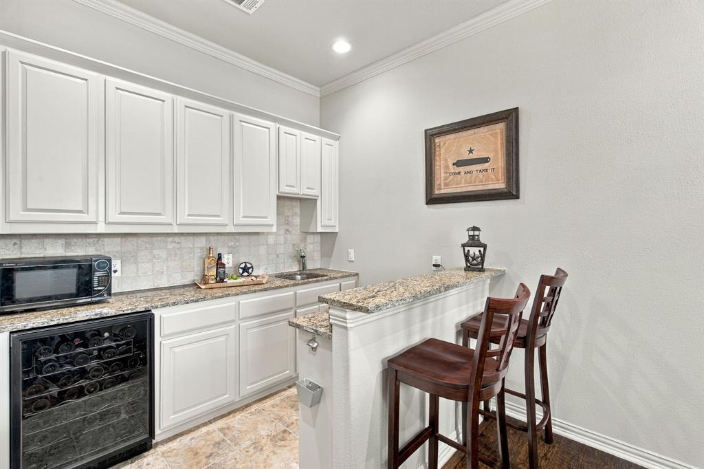 Wet bar featuring white cabinetry, stone-finish countertops, tile backsplash, built-in wine refrigerator, and sink