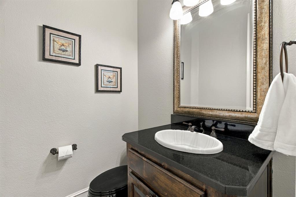Dark wood-finish vanity with a stone countertop, integrated oval undermount sink, multi-bulb vanity light fixture, and framed wall mirror